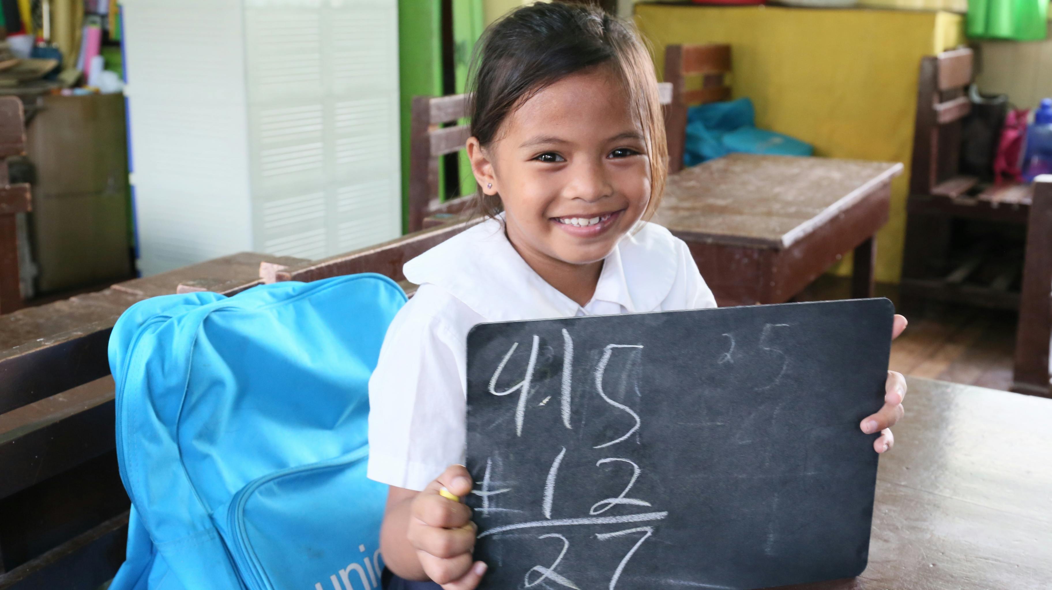 Flicka i Filippinerna håller i en svart tavla med siffror på